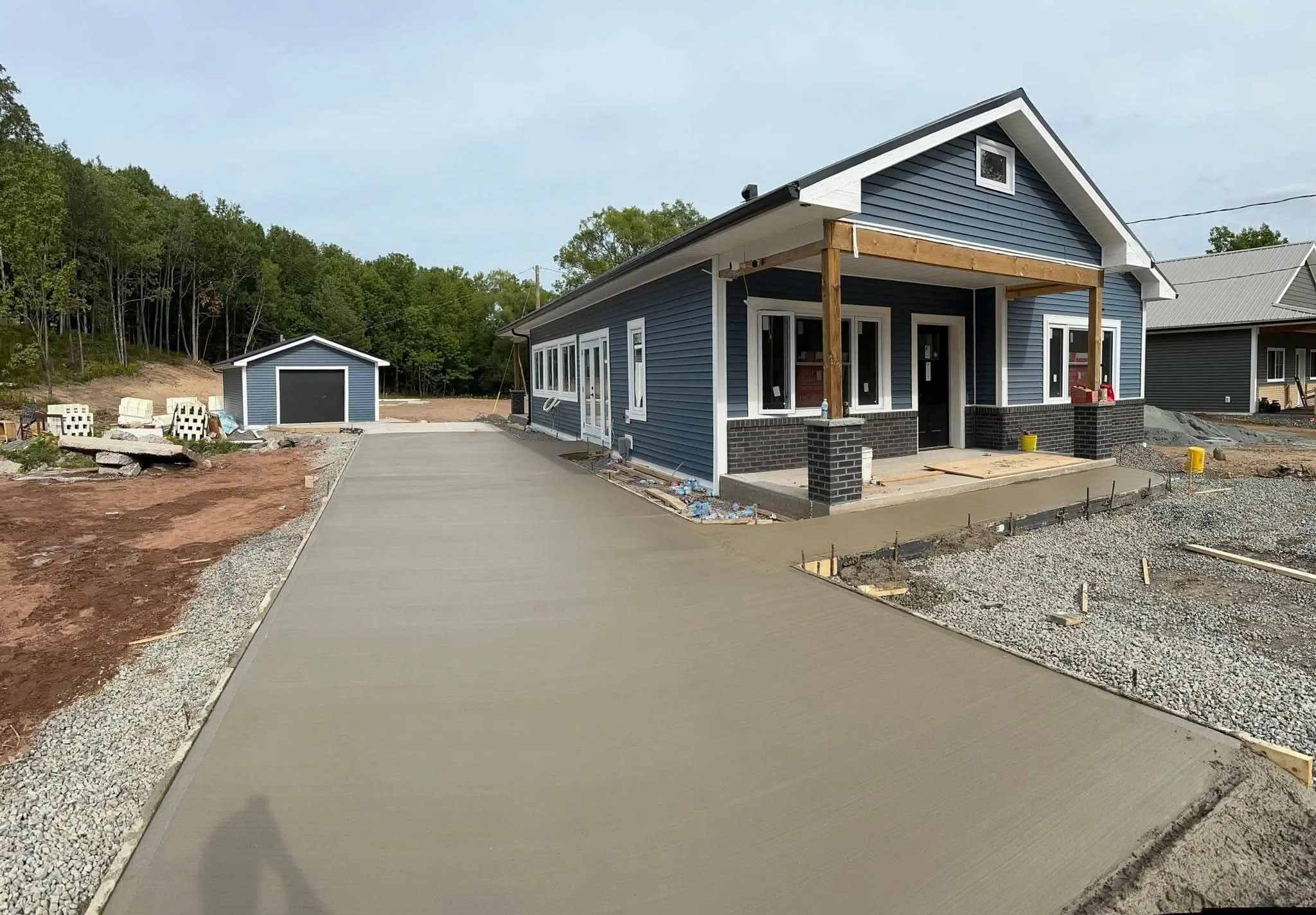 Freshly poured concrete driveway leading to a new blue house with a detached garage