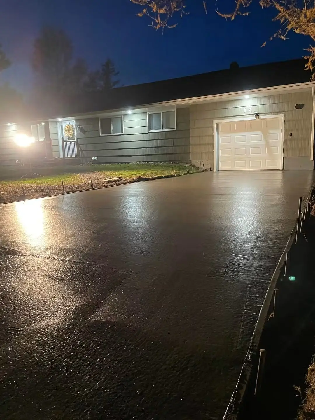 Concrete driveway being finished under work lights in front of a garage