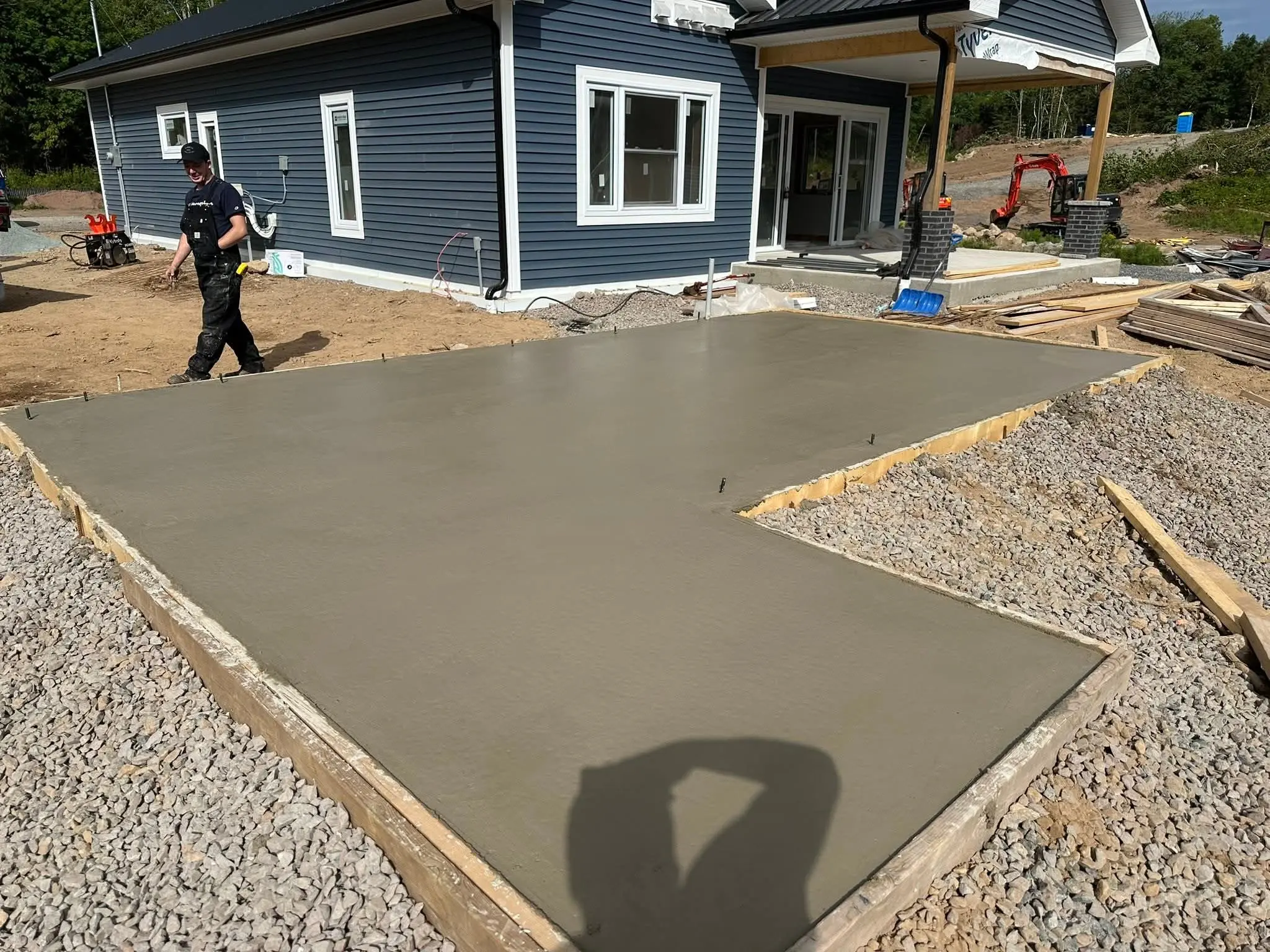 Langille crew finishing an L-shaped concrete pad beside a newly built blue house