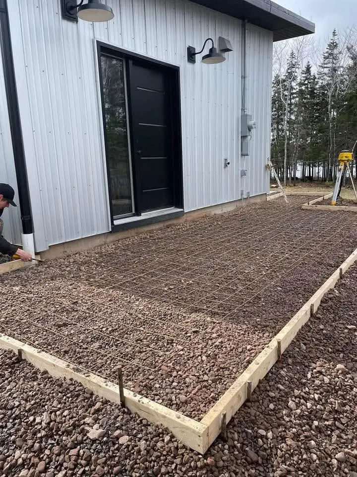 Gravel base and forms set behind a white board-and-batten house