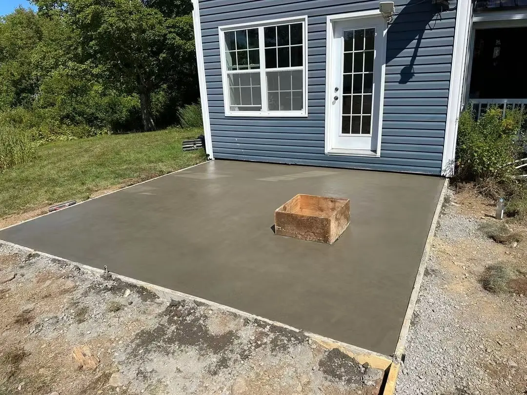 New concrete patio behind a blue house with a fire pit form in the centre