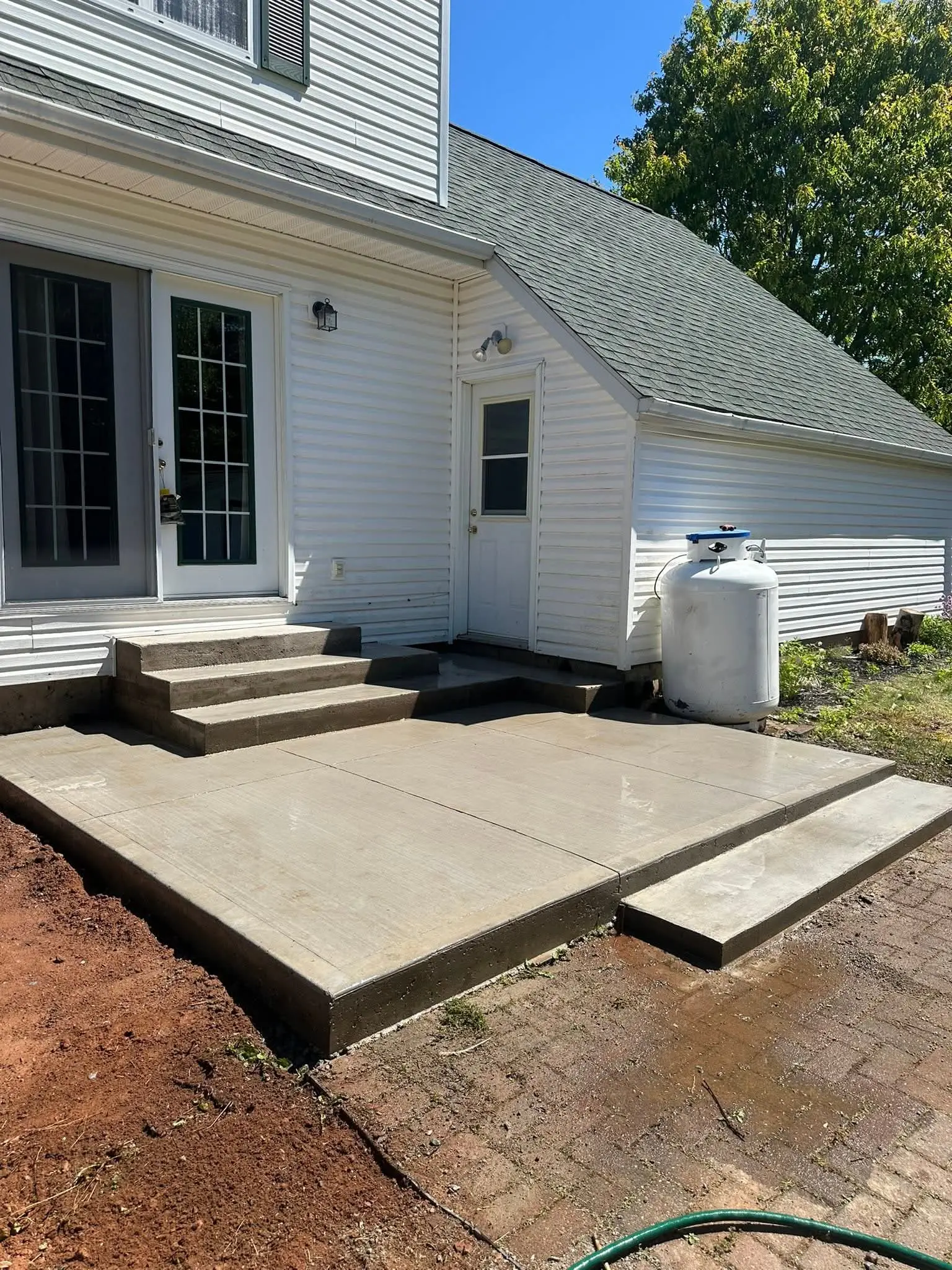 New poured concrete steps leading down to a concrete patio behind a white house