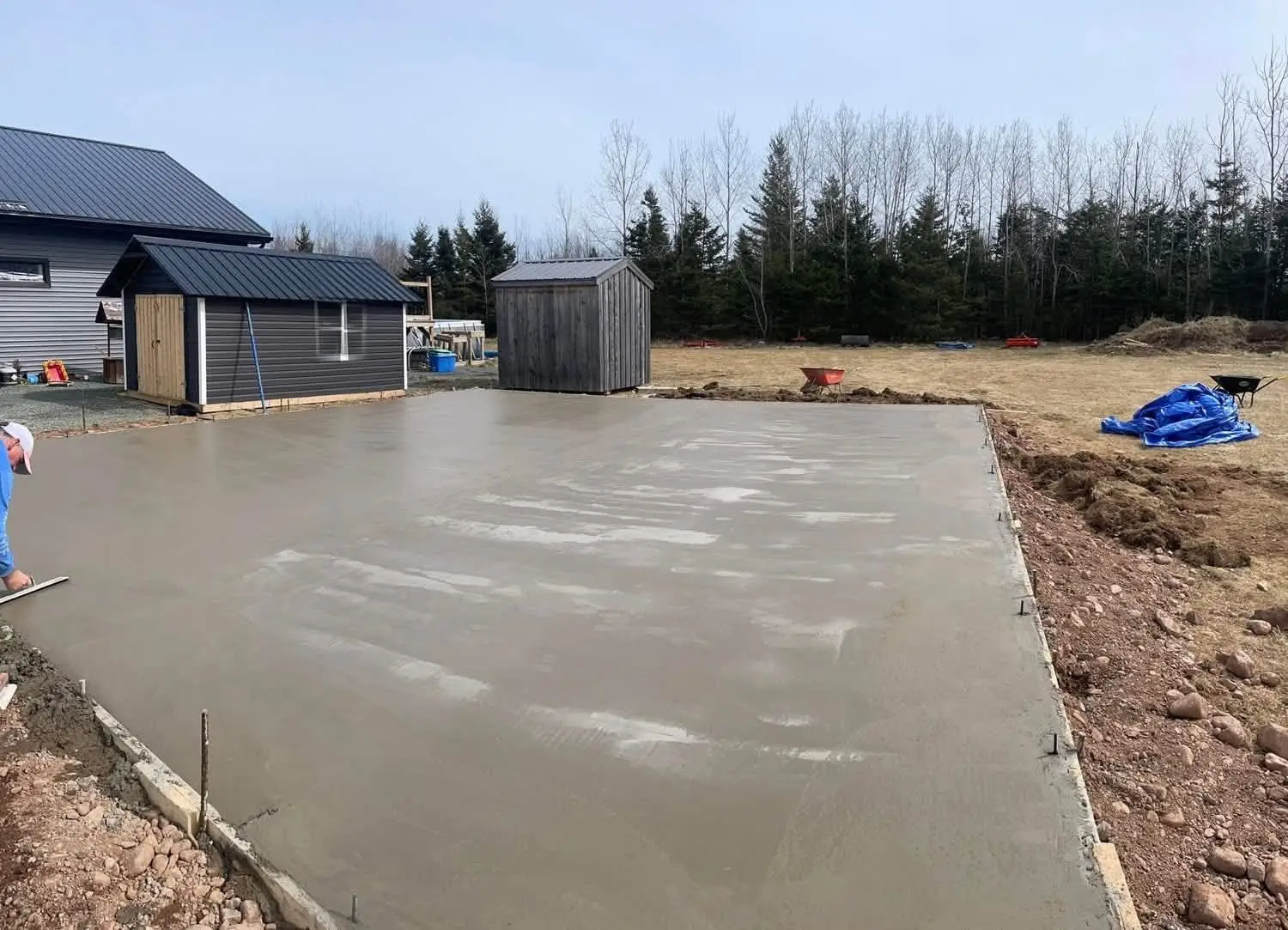 Freshly poured slab for a new outbuilding beside two sheds